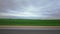 Highway along green meadows fields, cloudy weather in summer, overcast. Background. Overtaking passing of red passenger