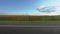 Highway along green meadows and plowed field in rural area. Electric power transmission towers on background. Overtaking