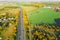 Highway between Autumn forest and cultivated ground with yellow trees at sunset in autumn. Aerial view of the traffic on speedway.
