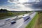 Highway in the country with driving cars and trucks in motion blur under a dramatic sky with clouds, concept for traffic,