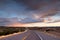 Highway curving into the distance through the landscape near Santa Fe, New Mexico underneath a dramatic colorful sky at sunset