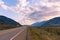 Highway running through valley with view of snow capped mountains at sunset