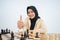Hijab woman with thumbs up while sitting playing chess