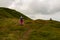 Hike backpacker lifestyle girl walking on trek trail in mountains outdoors with pink raincoat.