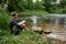 Hiker with a backpack and map sitting on the bank of a river and exploring of the area