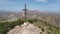 A hiker with a backpack reaches the summit cross near Orihuela.