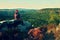 Hiker in black with red baseball cap on sharp cliff and watch to valley. Colorful summer day.