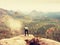 Hiker with camera on tripod takes picture from rocky summit. Alone photographer at edge photograph landscape