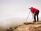 Hiker with camera on tripod takes picture from rocky summit. Alone photographer on summit