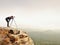 Hiker with camera on tripod takes picture from rocky summit. Alone photographer on summit