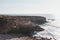 Hiker celebrates its success. Breathtaking cliffs with pebble beach in the afternoon sun on the Atlantic coast at Vila Nova de