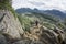 Hiker on Cliff High Above Small Town in Valley with Mountain Range in Distance