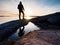 Hiker in dark sportswear with poles and sporty backpack. Coastline trail on rocky shore. Alone tourist enjoy