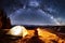 Hiker enjoying in his camp near the forest at night. Man sitting near campfire and tent under night sky full of stars