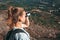 Hiker girl with backpack looking in binoculars enjoying spectacular view of valley on mountain top. Watcher tourist in travel