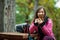 Hiker girl resting on a bench in the forest. Backpacker with pink jacket holding cell phone