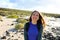 Hiker girl smiling at camera outdoors. Happy young traveler woman exploring Lanzarote hills and beaches in a sunny and windy day.