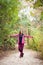 Hiker girl standing on a wide trail in the mountains. Backpacker with pink jacket in a forest. Healthy fitness lifestyle outdoors