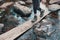 Hiker girl wades across the river on wooden Board, heavy Hiking boots