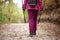 Hiker girl walking away from camera on a wide trail in the mountains. Back view of backpacker with pink jacket in a forest.
