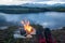 Hiker with hiking boots are relaxing by bonfire outdoors with lake and mountain view