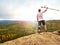 Hiker with knee joint stability bandage and forearm poles. Hiker on the cliff makes triumph gesture. Hilly landscape