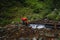 Hiker on a long trail refills drinking water from a mountain spring into a glass container. Replenishing clean water for cooking