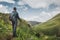 Hiker Man With Backpack And Trekking Poles Resting And Looking At The Mountains In Summer Outdoor, Rear View