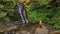 hiker man in yellow raincoat enjoying the view of waterfall in the forest