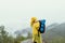 Hiker man in a yellow raincoat stands on top of a mountain in rainy weather against the backdrop of foggy views of the forest and