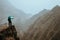 Hiker with map in steep rocky terrain in front of a incredible panorama view of high mountain ranges deep ravines and