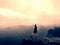 Hiker in pants is taking photo on the rocky peak at sunrise. Mist in rocky mountains