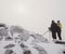 Hiker and photo enthusiast stay on snowy peak at tripod. Men on cliff speaking and thinking.