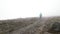 Hiker with a pole walking down a stony mountain slope in foggy windy weather. Clip. Lonely tourist descending a hill.