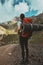 Hiker with red backpack is standing on top of a mountain and enjoying camping valley view