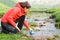 Hiker in red filling canteen in a creek in the mountain