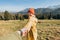 Hiker with red hat stands on edge of cliff against background and extends a hand. Happy woman gives a hand to someone