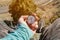 Hiker sitting on a high rock holds a compass in front of her feet in trekking boots and a high cliff with an asphalt