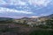 Hiker are standing on a mountain top with green tent infront. Purple and pink skies overhead and cotton flowers infront.