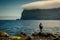 Hiker standing at the rocky shore near Mikladalur village looking at the Kunoy island, Kalsoy island, Faroe Islands