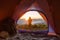 The hiker stands at the front orange camping tent and backpack in the mountains.