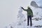 Hiker with a walkie-talkie peers into the distance, standing on top of a mountain during a snowstorm