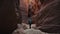 Hiker Walking On Dry Curve Riverbed In Deep Slot Canyon With Orange Smooth Rocks