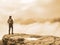 Hiker watching over misty valley to blurred horizon in thick fog