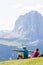 Hikers rest on the lawn admiring the Sassolungo mountain which is part of the Dolomites, Euro