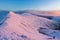 Hikers on the summit of a snow covered mountain bathed in pink dawn light