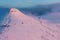 Hikers on the summit of a snow covered mountan bathed in pink dawn light