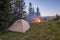 Hikers tent in mountains at evening with a bonfire with sparkles