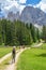 Hikers on a trail at an alpine meadow with high mountain peaks