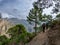 Hikers walking along narrow path with pine trees and mountains of Sierra de Tejeda and Almijara in the background with cloudy